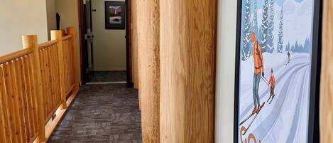A hallway with wooden beams, a carpeted floor, and a framed poster of a skiing scene.