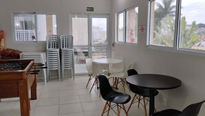 Una habitación con mesa de fútbol, sillas de plástico, una mesa redonda y vistas a través de las ventanas.
