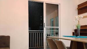 Una habitación con puerta corrediza de vidrio que da a un balcón, una mesita con sillas y una planta en maceta.
