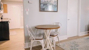 Un coin repas avec une table ronde en bois et deux chaises blanches, un tableau encadré au-dessus de la table et un panneau « interdiction de fumer » sur le mur.