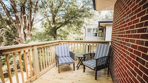Une terrasse en bois avec deux chaises à rayures et une petite table, entourée d’un mur de briques et d’arbres.