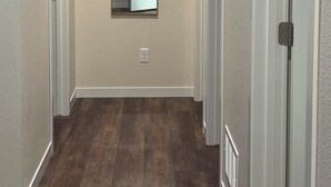 A hallway with a wooden floor, a mirror on the wall, and a door on the right.
