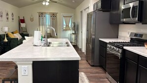 A modern kitchen with a central island, stainless steel appliances, and a dark wood floor.