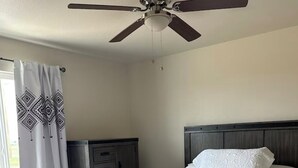 A bedroom with a bed, a ceiling fan, a dresser, and a window with curtains.