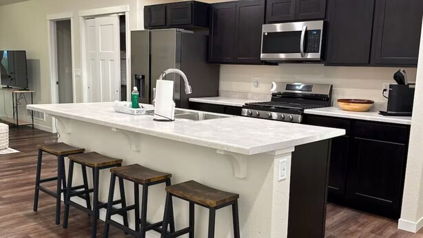 A modern kitchen with dark cabinets, a white island with bar stools, and a stainless steel range hood.