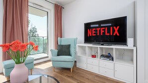 A modern living room with a large flat-screen TV displaying "NETFLIX," a teal armchair, a pink vase with flowers, and a white entertainment unit. - Luxury apart for family near Księży Młyn (Łódź)
