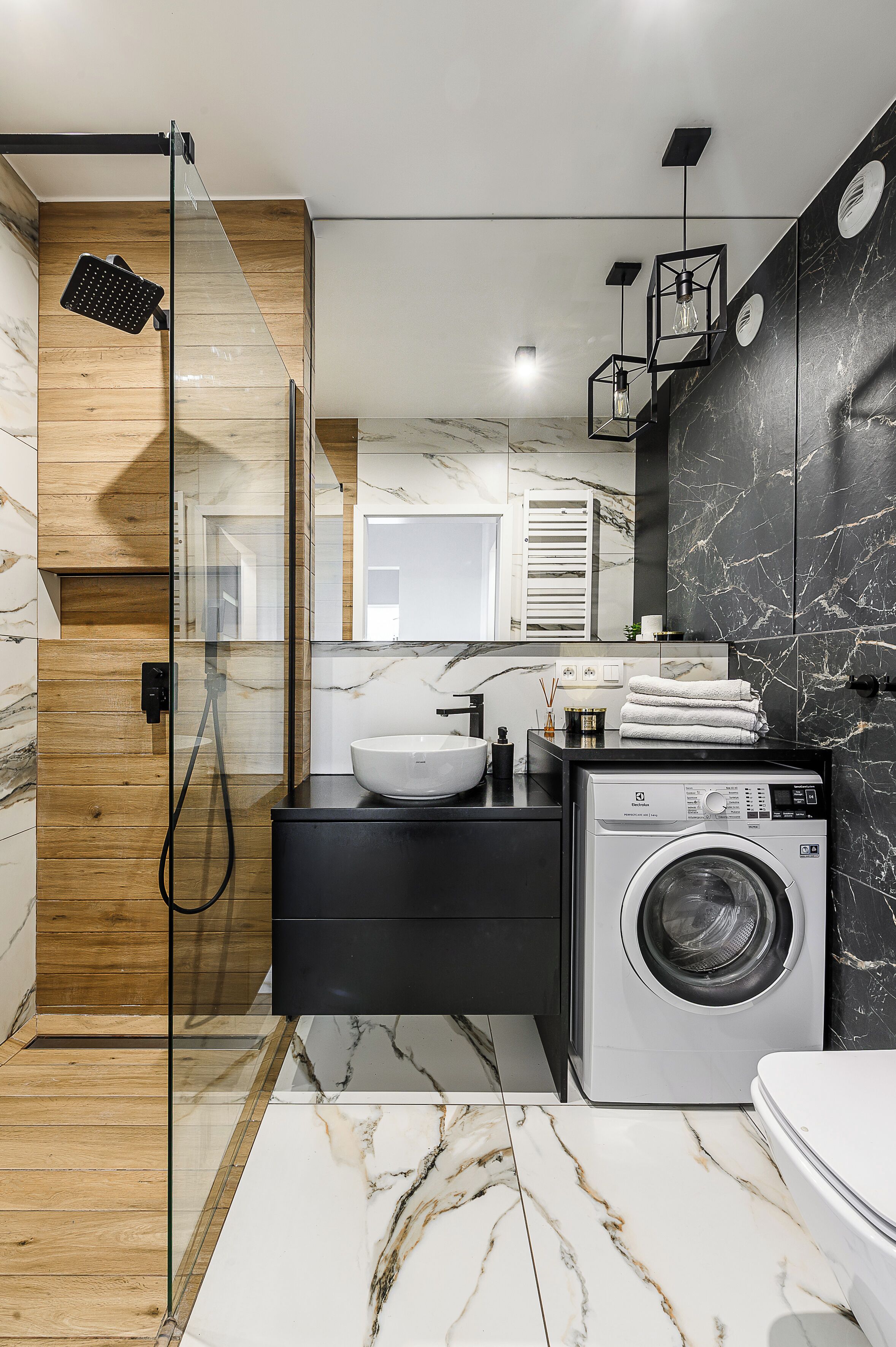A modern bathroom with a glass shower enclosure, a sink, a washing machine, and a towel rack.