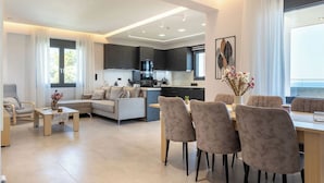 A modern living room with a sofa, coffee table, and dining area with chairs. - Villa Calissea (Agia Pelagia)