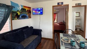 Una sala de estar con un sofá azul oscuro, un televisor de pantalla plana montado en la pared y un comedor con una mesa preparada para dos.