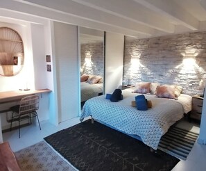 A bedroom with a large bed, a desk, a chair, and a mirror.