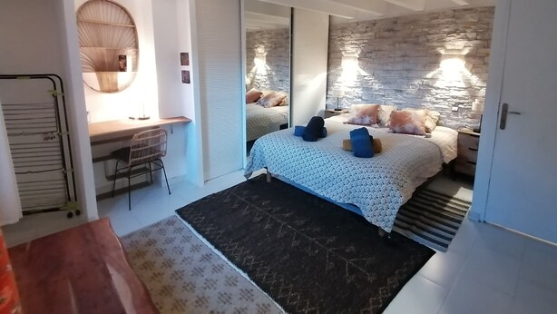 Une chambre avec un lit, un bureau, un miroir et un mur en pierre.