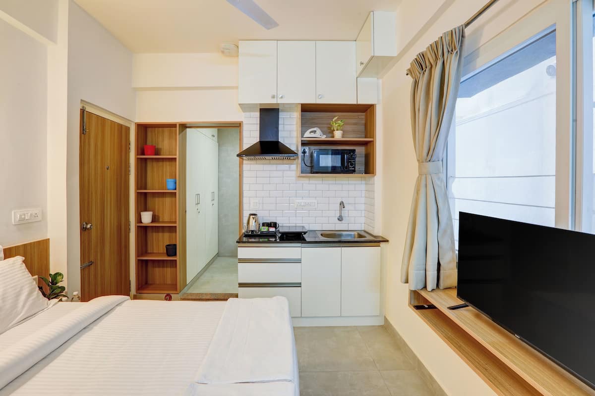 Una habitación de hotel compacta con kitchenette, cama, televisor y baño.