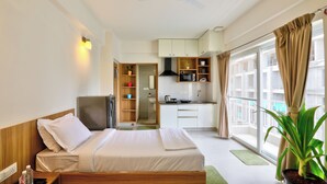 A hotel room with a bed, a TV, a kitchenette, and a large window with curtains. - Acasa Suites ITPL Whitefield (Bengaluru)