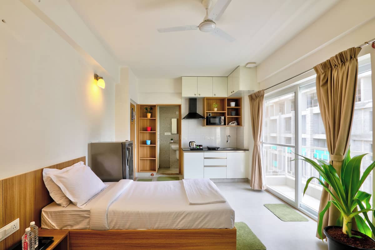 Una habitación de hotel con cama, televisión, kitchenette y un ventanal con cortinas.