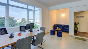 A modern office with a large table, chairs, computers, and a blue sofa. - Acasa Suites ITPL Whitefield (Bengaluru)