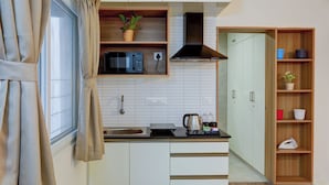 A kitchen with a microwave, stove, and wooden shelves. - Acasa Suites ITPL Whitefield (Bengaluru)