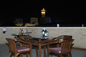 An outdoor dining area with a table and chairs, a brick wall, and a view of a tower in the background. - Sarroj  (Bukhara)