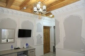 Habitación de hotel con techo de madera, un candelabro, televisor de pantalla plana, un espejo y una puerta de madera.