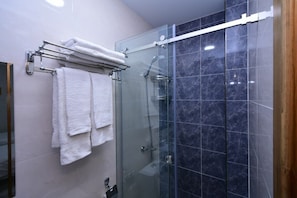 A glass-enclosed shower stall with a marble tile wall, a towel rack with folded towels, and a visible shower control panel. - Sarroj  (Bukhara)