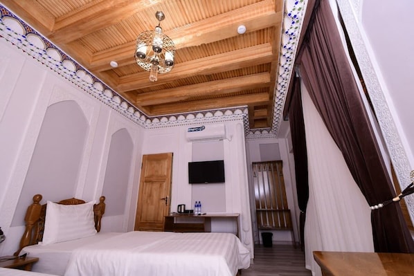 Una habitación de hotel con techo de madera, una cama, un escritorio, un televisor y una puerta que da a otra habitación.