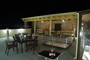 Un patio al aire libre con una mesa y sillas, una zona de estar cubierta con bancos y una barandilla.