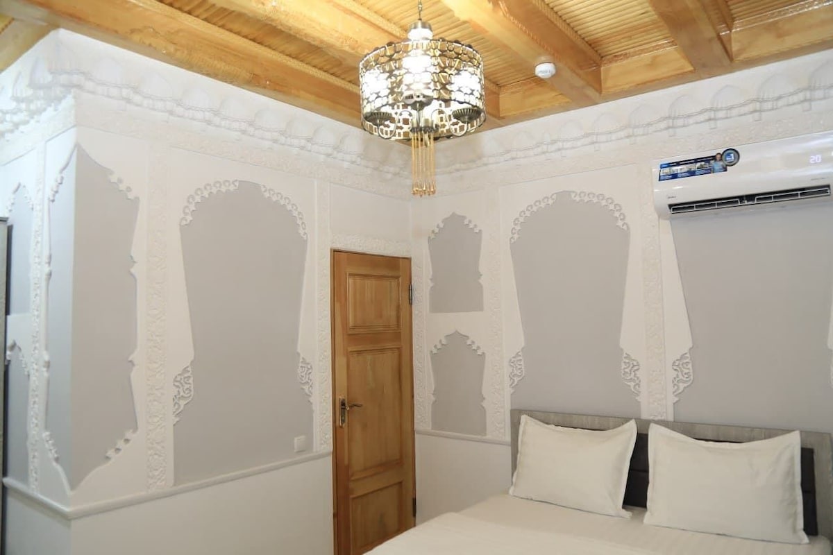 A bedroom with a bed, a chandelier, an air conditioning unit, and a wooden door.