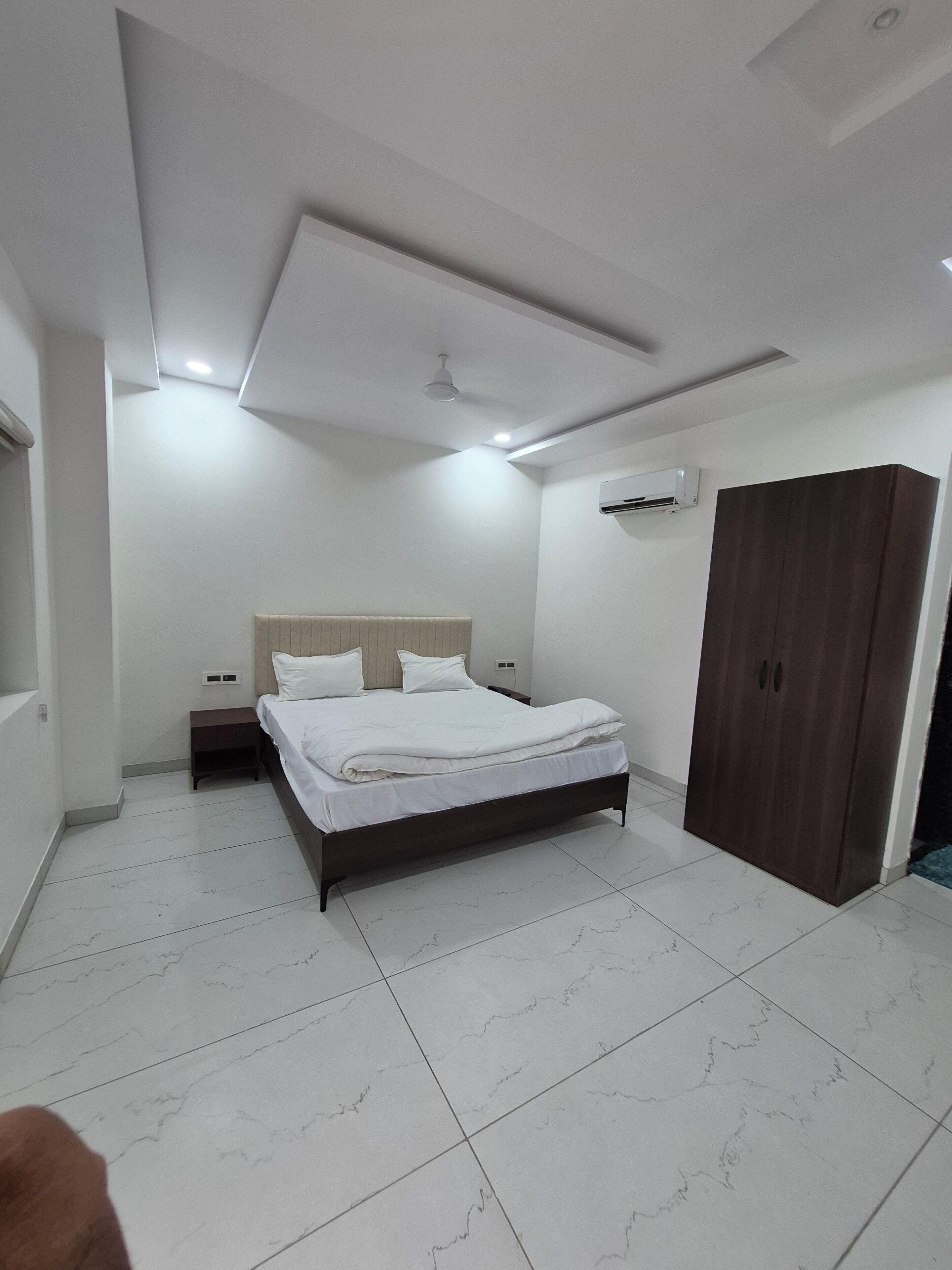 A modern bedroom with a large bed, a wardrobe, and an air conditioning unit.