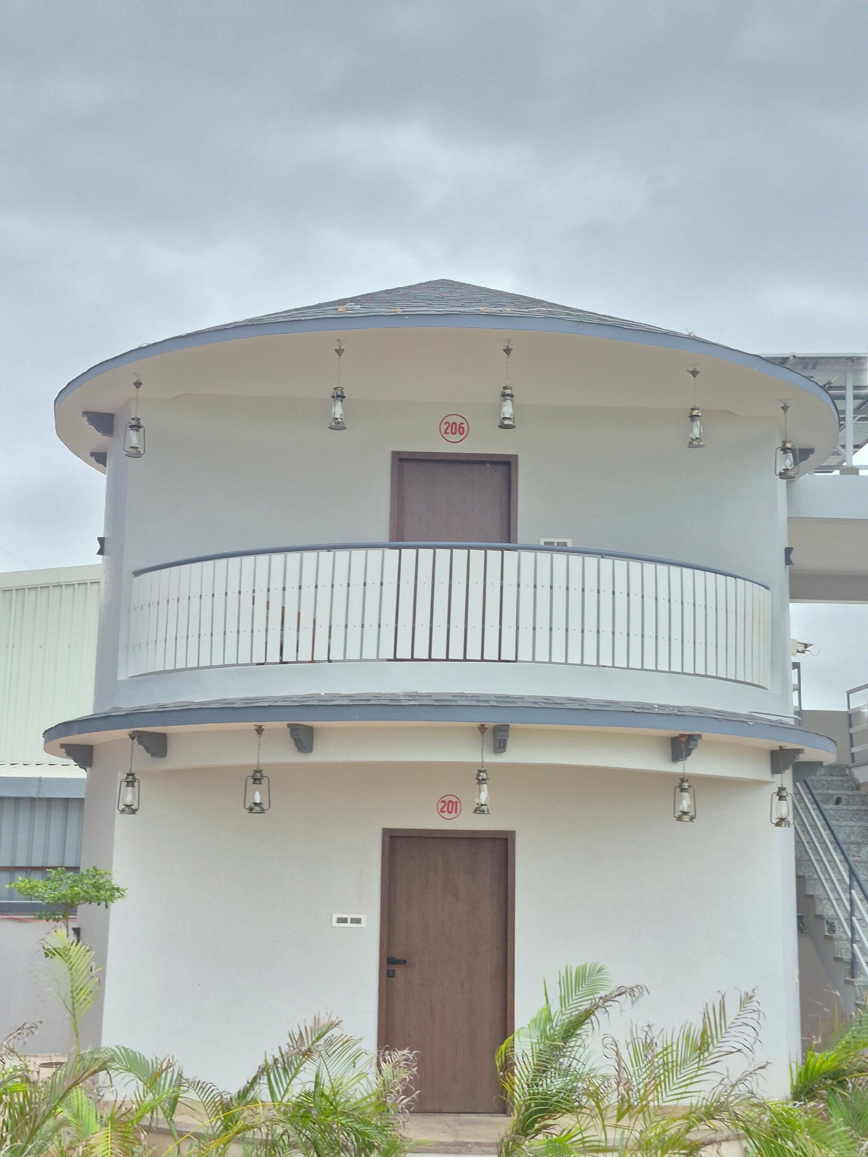 A cylindrical building with a balcony, a door, and two visible room numbers (206 and 201).