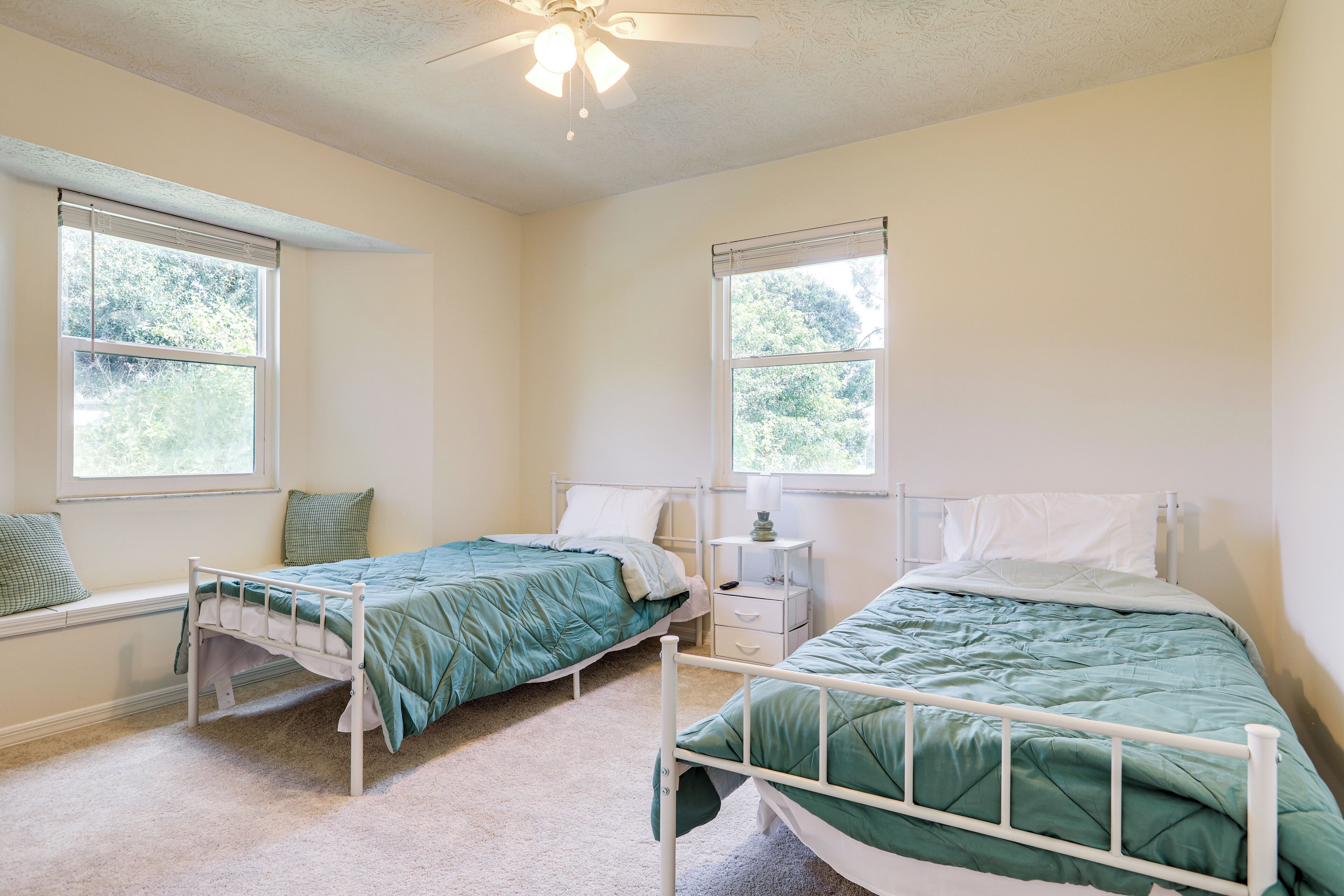 A bedroom with two single beds, a nightstand, and a window with blinds.