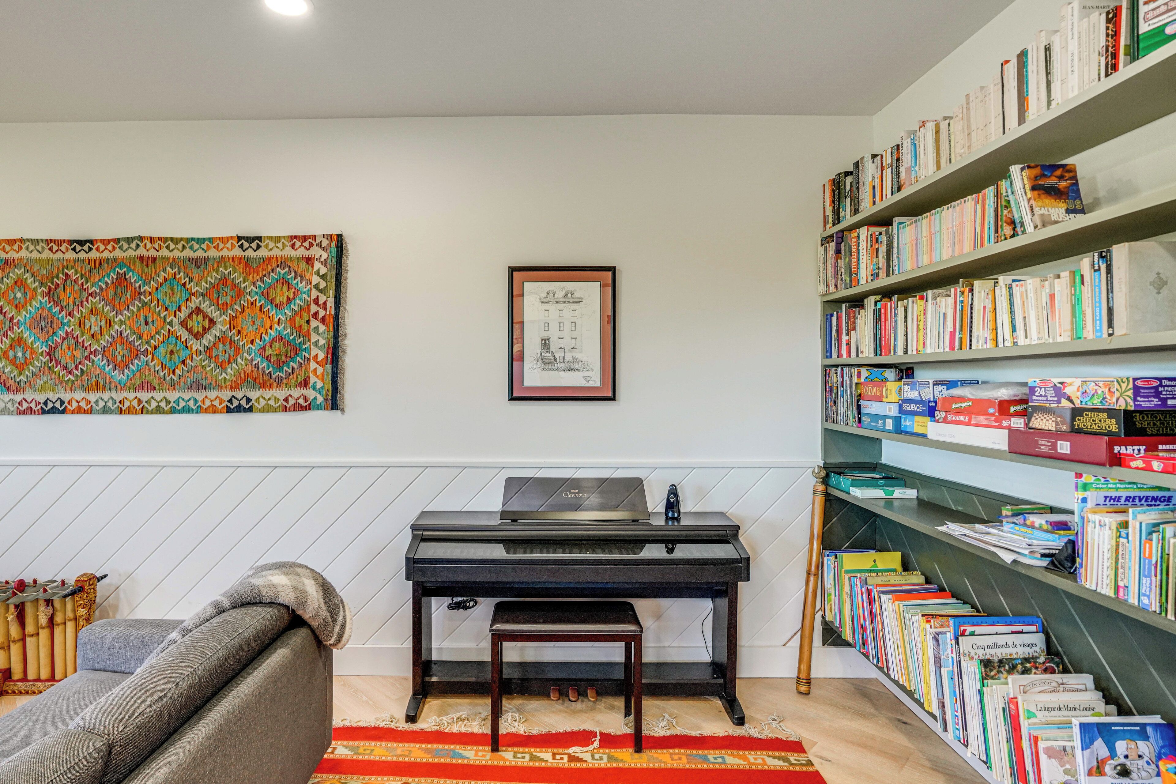 A room with a piano, a bookshelf filled with books, a framed picture on the wall, and a colorful rug.