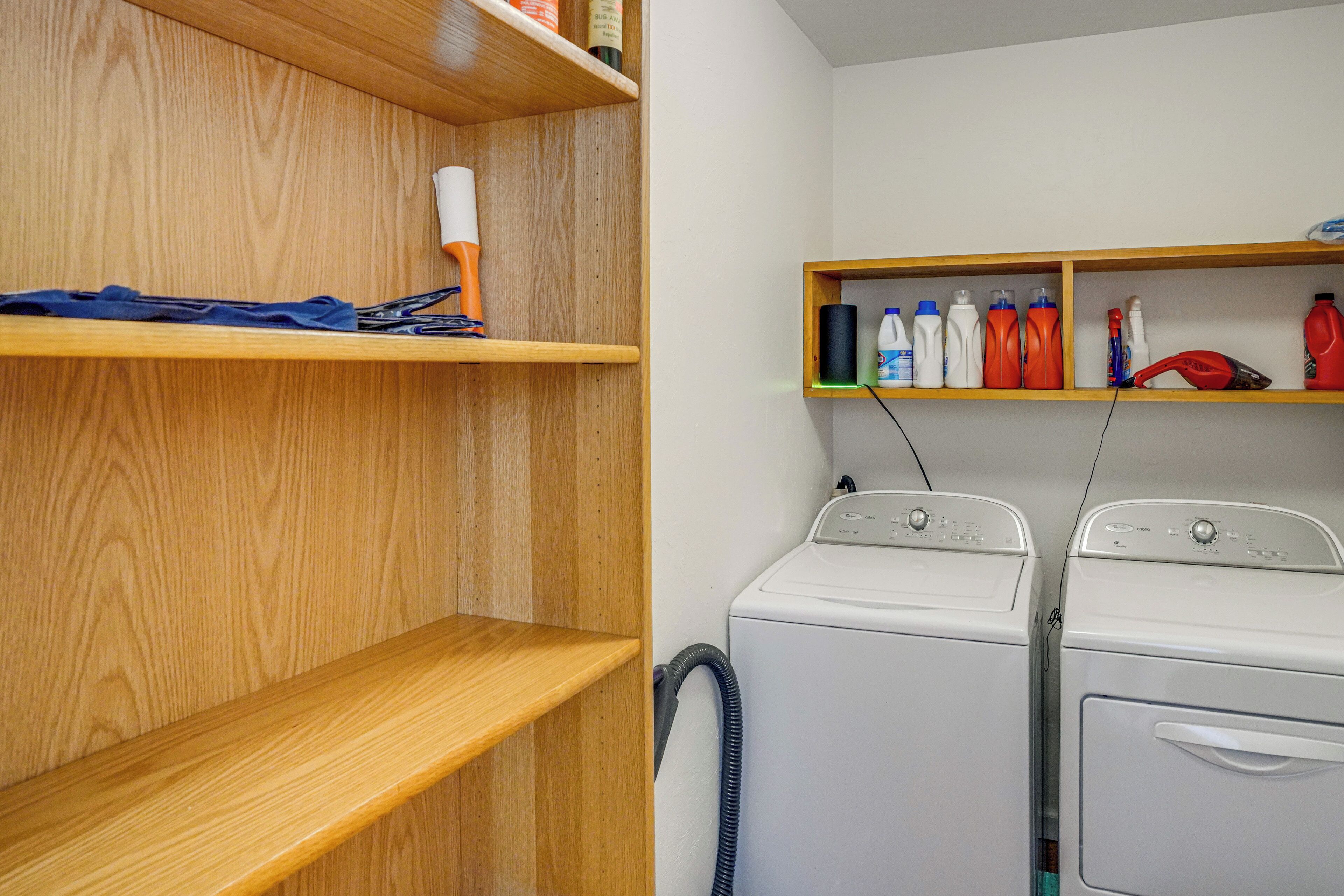 A laundry area with two white washing machines, wooden shelves with cleaning supplies, and a blue towel on the left shelf.