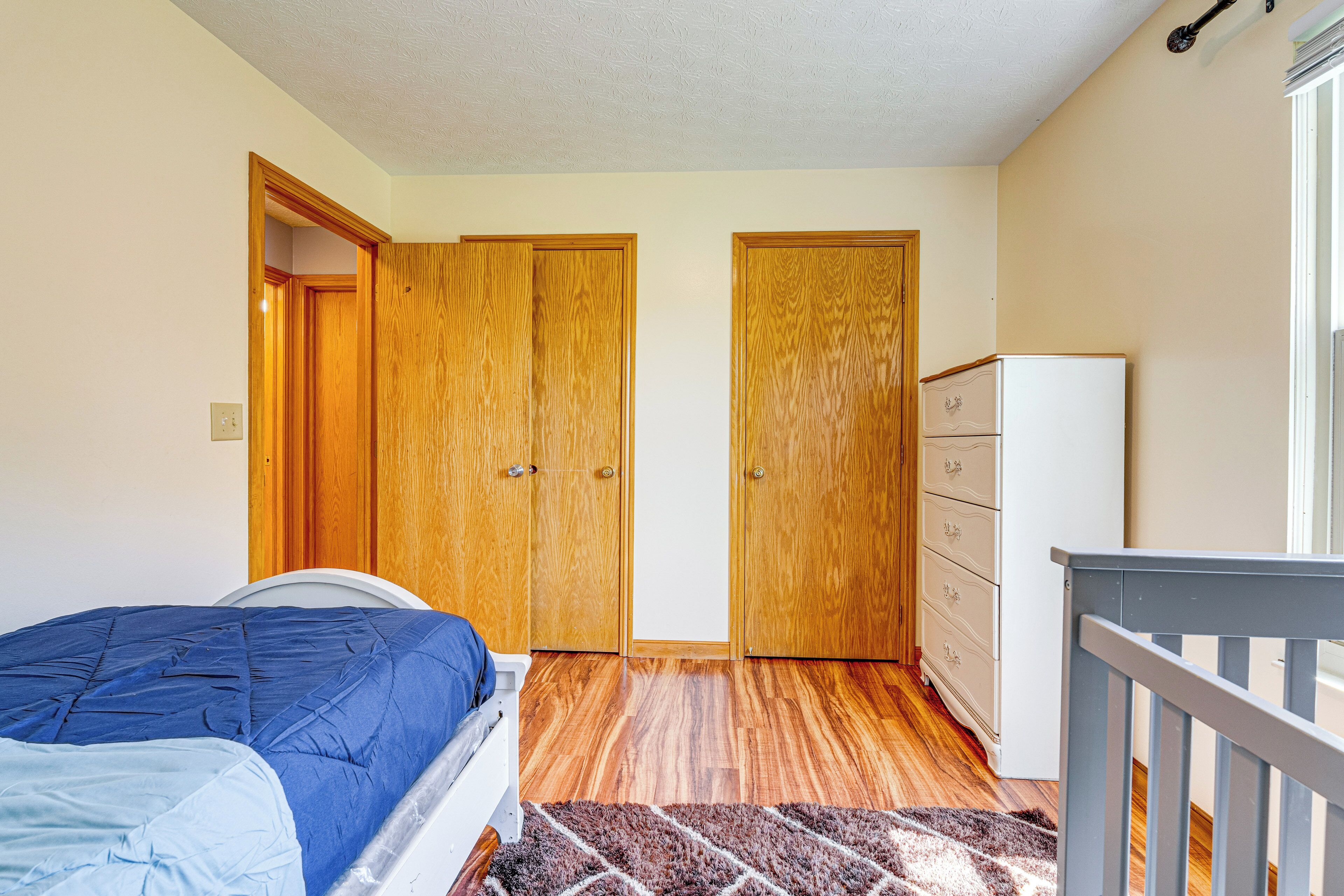 A bedroom with a bed, wooden wardrobe, dresser, and a small white refrigerator.
