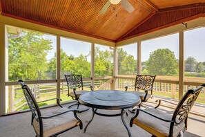 A covered patio with a round table and four chairs, large windows, and a wooden ceiling. - Families Welcome: Lake-view Home, 2 Mi to Gahanna! (Columbus)