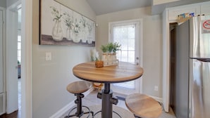 A kitchen with a round wooden table, two stools, a refrigerator, and a painting of vases on the wall.