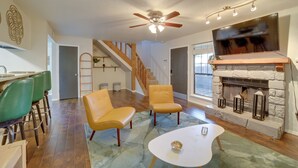 A spacious living room with a fireplace, a ceiling fan, and a television mounted above it. - 10 Mi to Dtwn Tulsa: Condo w/ Pool Access! (Tulsa)