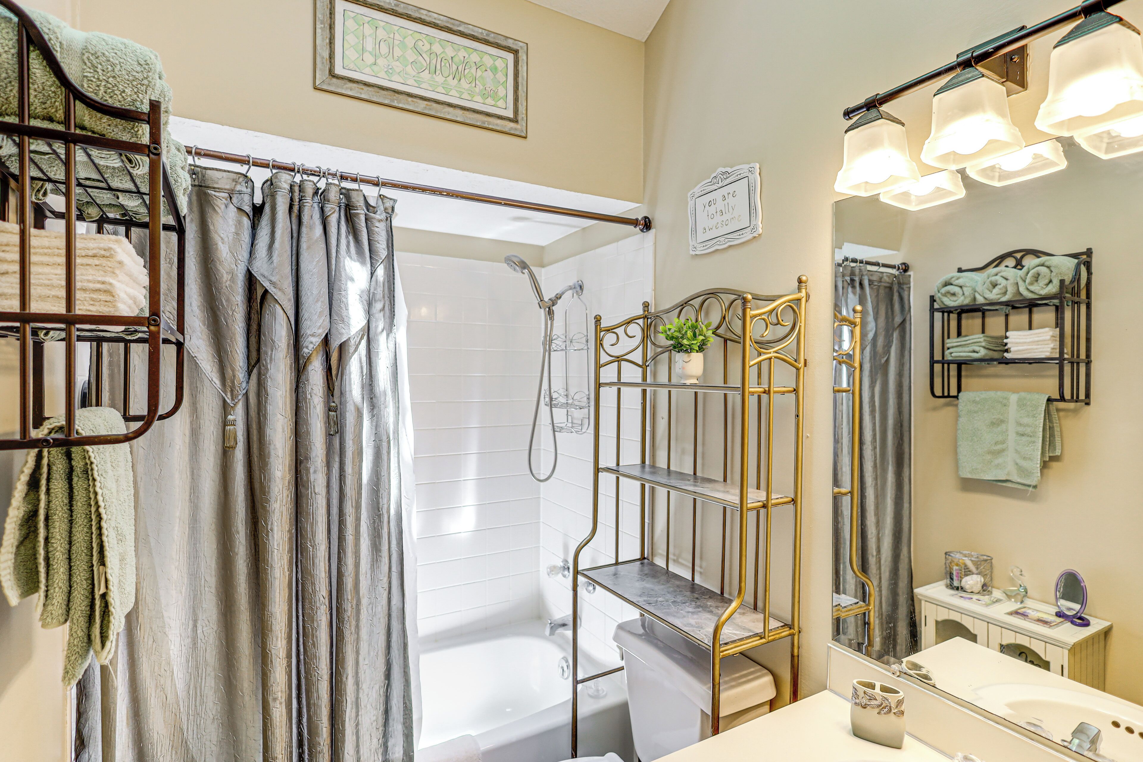 A bathroom with a shower, a toilet, a sink, and a mirror. There are towels and a plant on shelves.