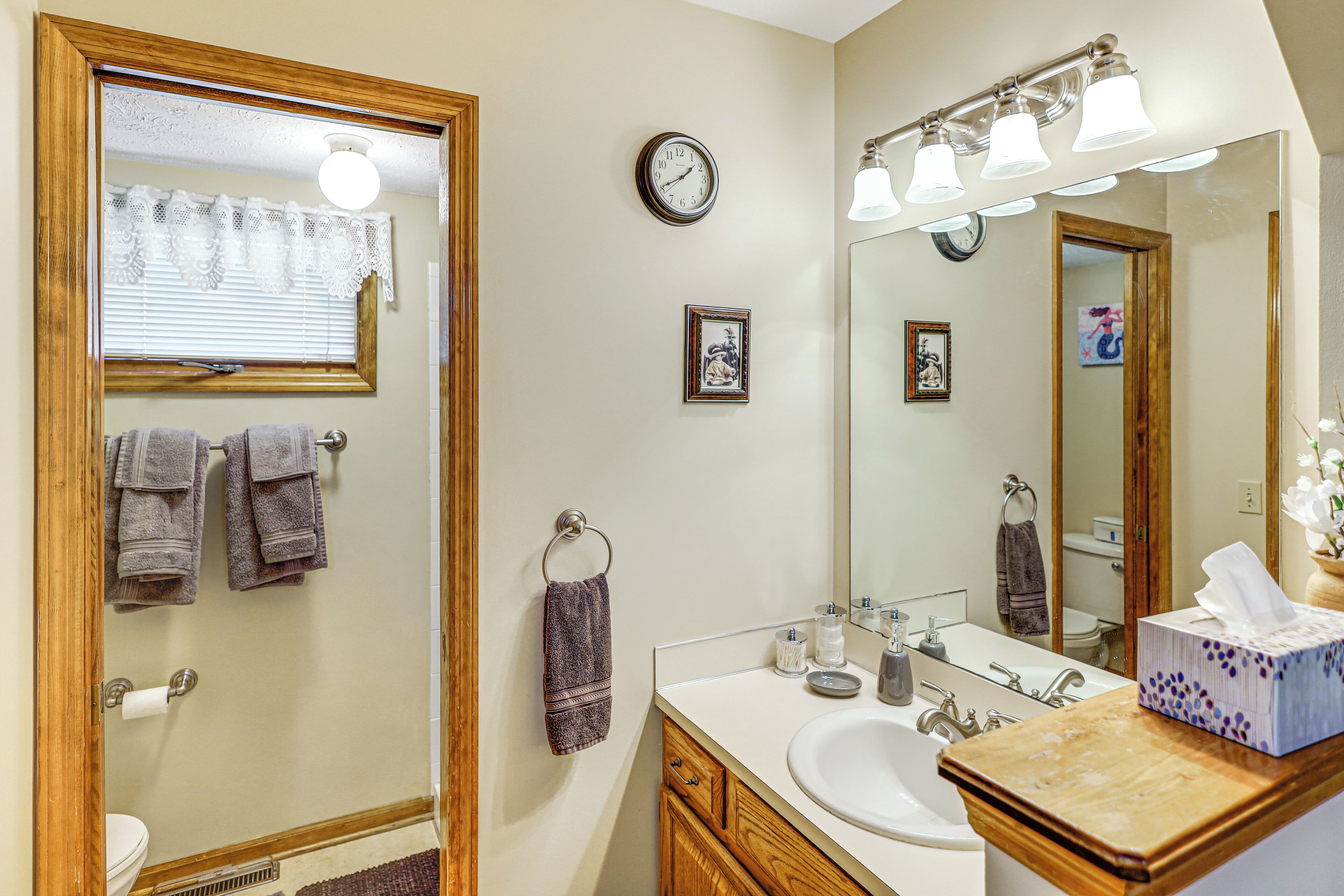 A bathroom with a wooden vanity, a sink, a mirror, and a clock on the wall.