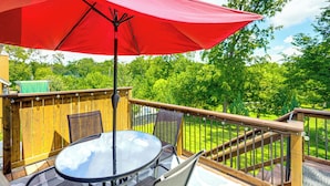 A wooden deck with a glass table and chairs, a red umbrella, and a view of a green lawn and trees. - 5 Mi to Platte River: Inviting Bellevue Rental (Bellevue)