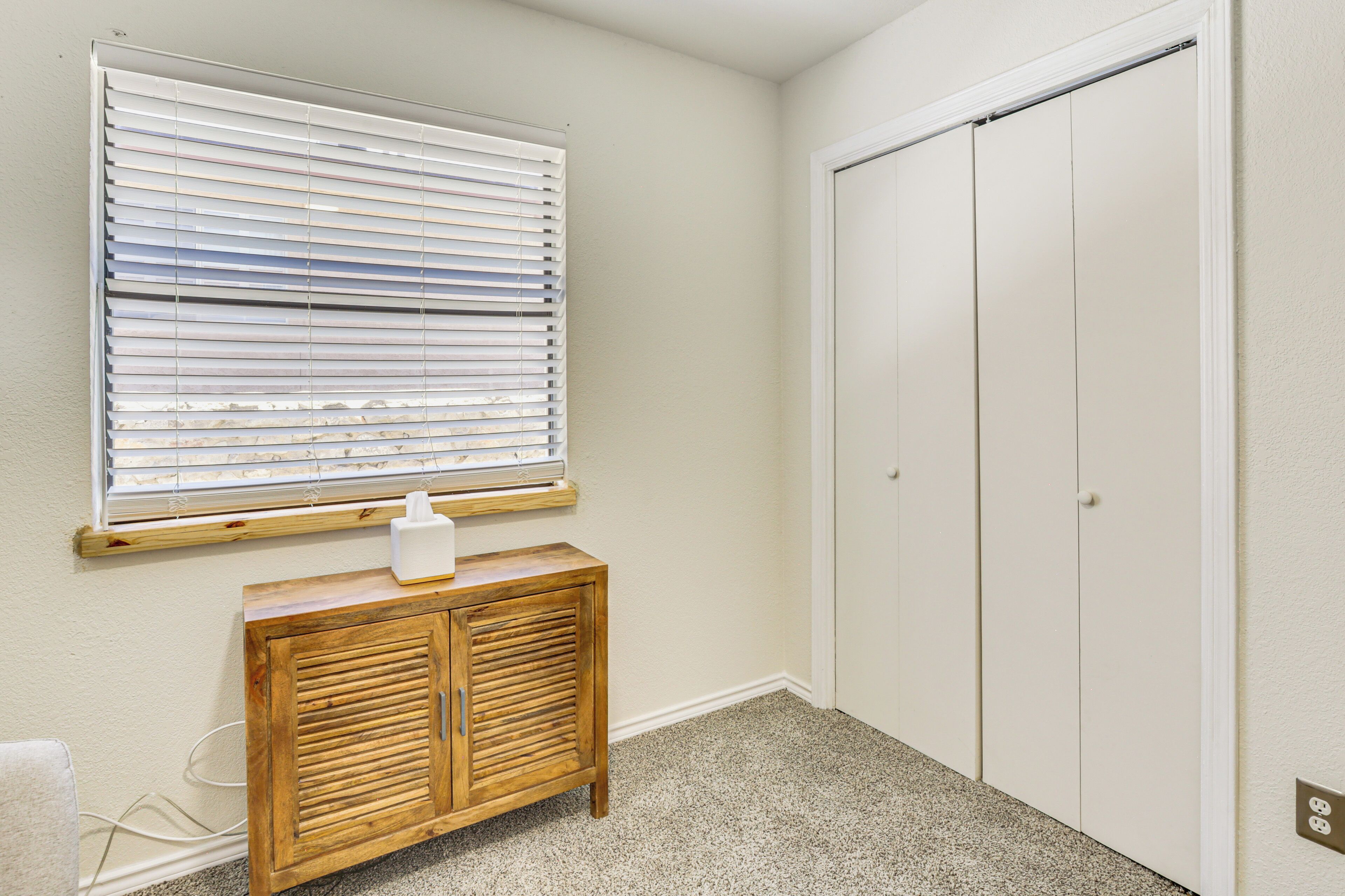 A room with a wooden cabinet, a window with blinds, and a white closet.