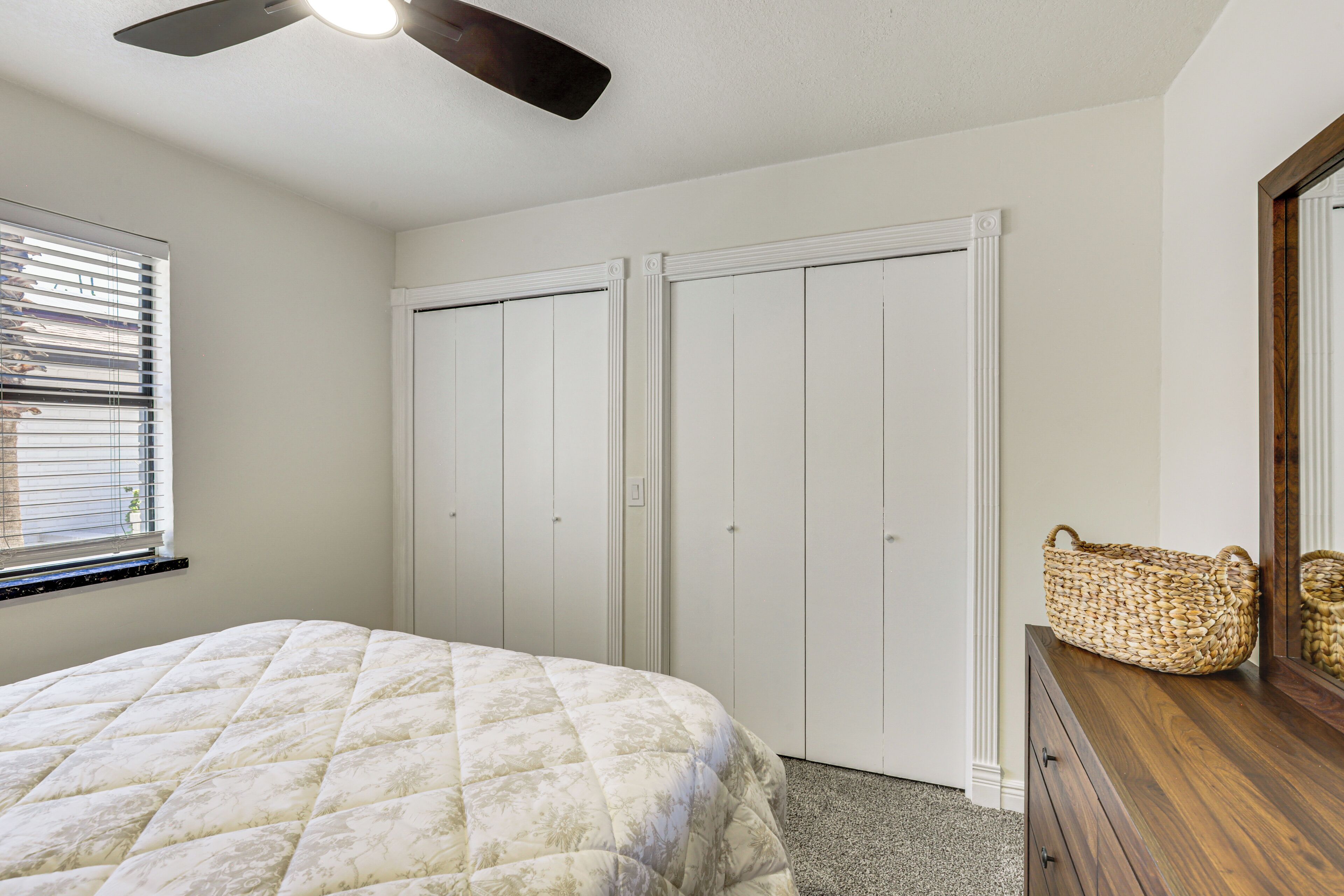 Une chambre à coucher comprenant un lit, une commode, un ventilateur de plafond et un placard aux portes blanches.