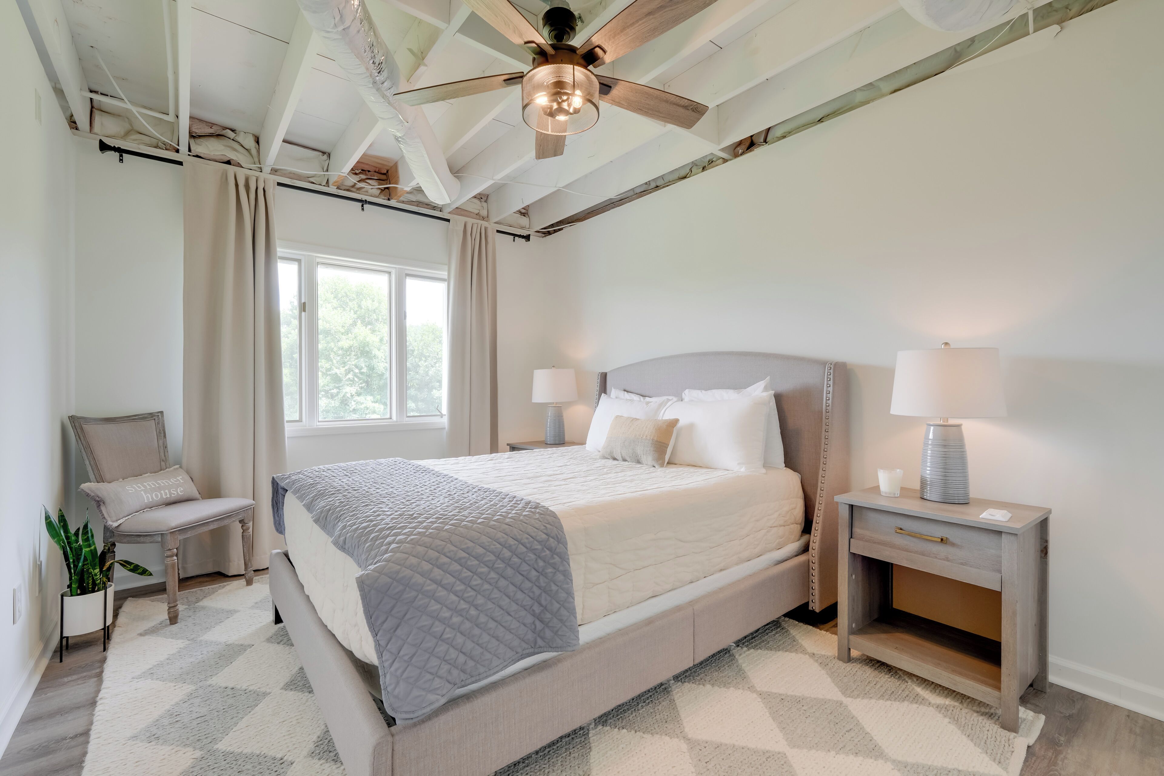 A bedroom with a bed, nightstands, a chair, a ceiling fan, and a window.