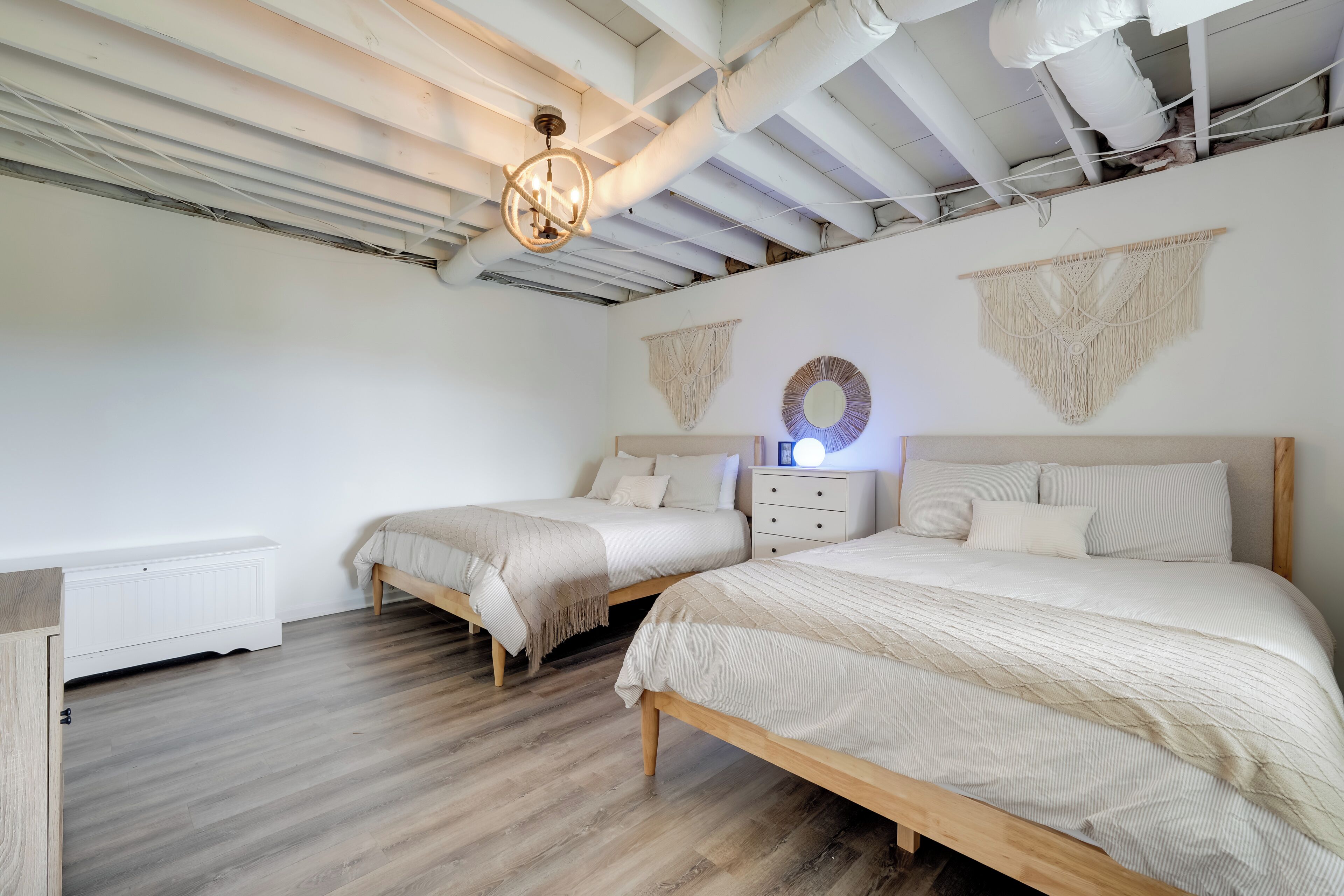 A bedroom with two beds, wooden flooring, a white radiator, and a ceiling with exposed pipes.