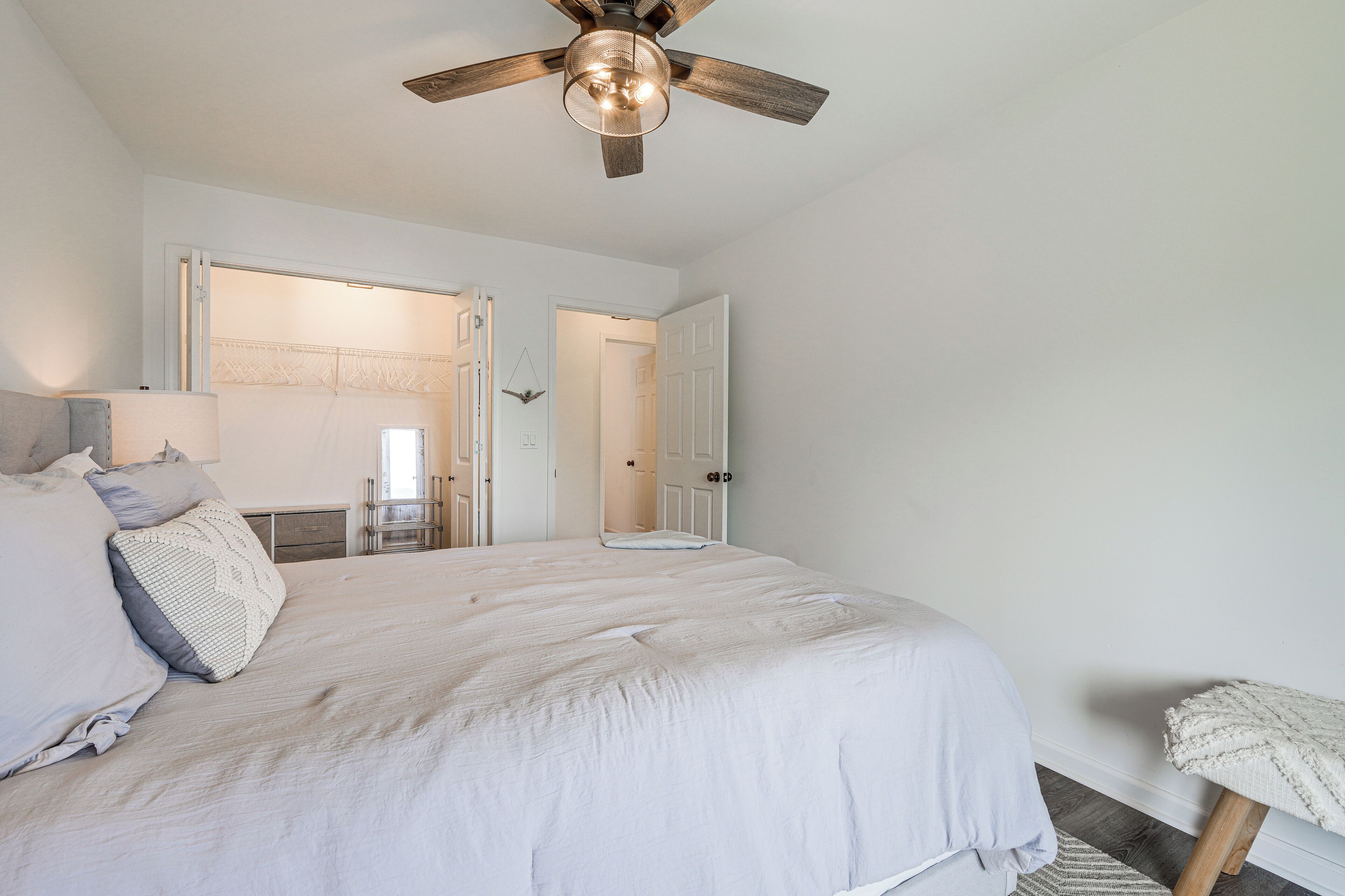 A bedroom with a large bed, a ceiling fan, and a view of a bathroom through an open door.