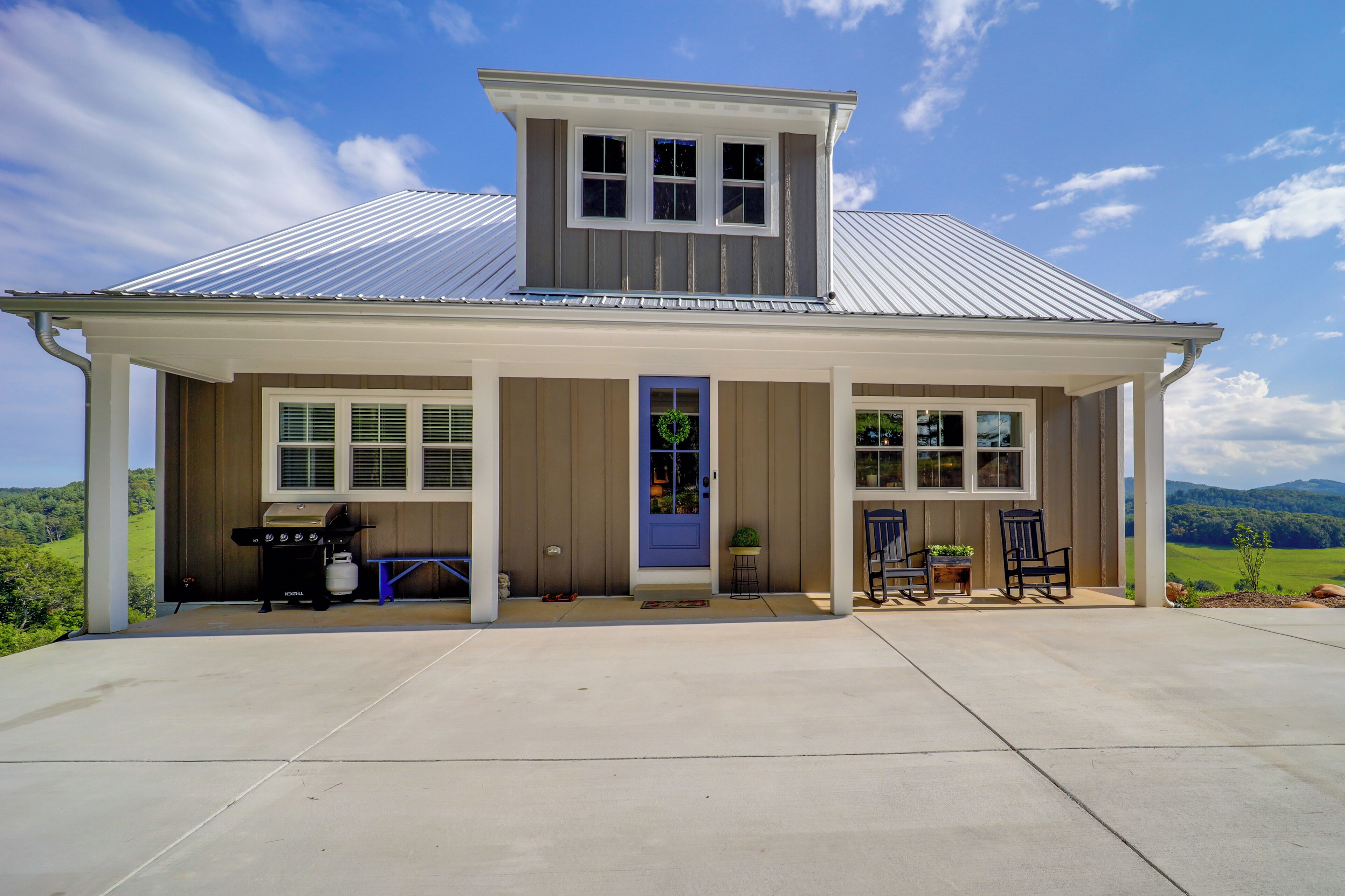 A two-story house with a covered porch, a blue door, and a barbecue grill outside.