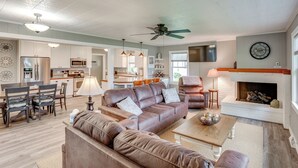A spacious living room with a fireplace, leather sofas, and a dining area with a chandelier. - Bring Your Boat! Little Traverse Lake Getaway (Maple City)