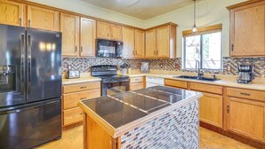 A kitchen with wooden cabinets, a black refrigerator, a stove, and a tiled backsplash. - Southwestern Chic! Tucson Retreat w/ Private Patio (Tucson)