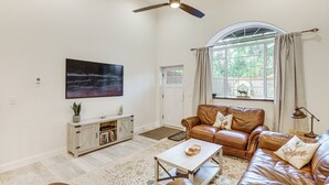 A living room with leather sofas, a coffee table, a bookshelf, and a large window with curtains. - Joliet Main Street Retreat < 30 Mi to Red Lodge (Joliet)