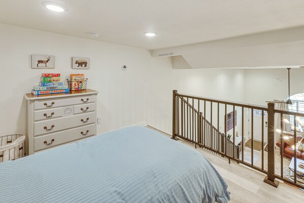 A bedroom with a bed, dresser, and a staircase leading to a balcony. - Joliet Main Street Retreat < 30 Mi to Red Lodge (Joliet)