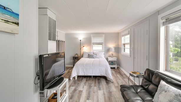 Een slaapkamer met een bed, een televisie, een leren bank en een raam met uitzicht op groen.