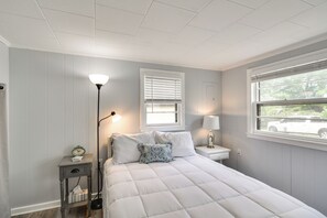 A bedroom with a bed, bedside tables, a lamp, a clock, and a window with blinds.